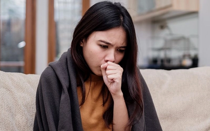 Một người đang bị ho và khó chịu, hình ảnh liên quan đến các bệnh hô hấp do thời tiết ẩm.