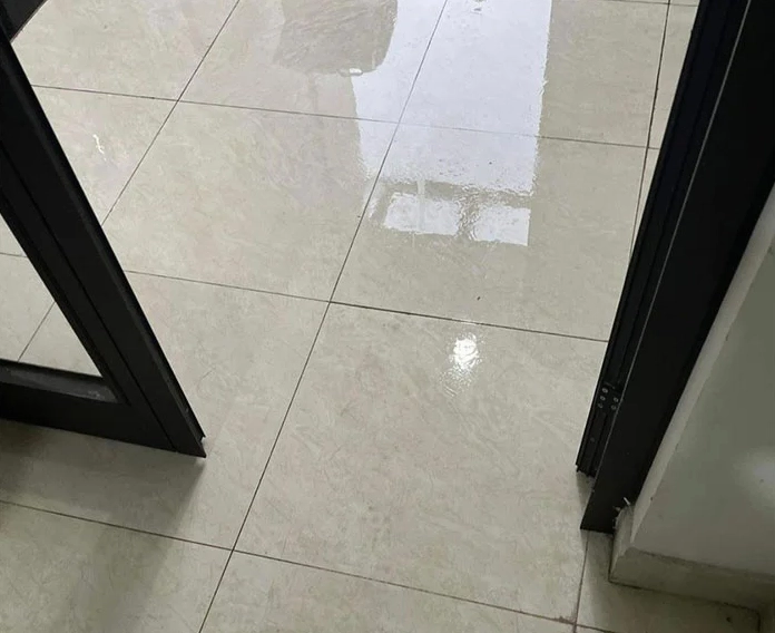 Sàn nhà gạch men bóng loáng nhưng đọng đầy nước do hiện tượng nồm ẩm.